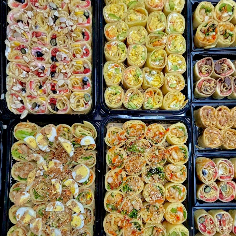 Assorted savory and sweet tortilla roll-ups arranged in black trays, featuring vegetables, meats, eggs, berries, and sauces.