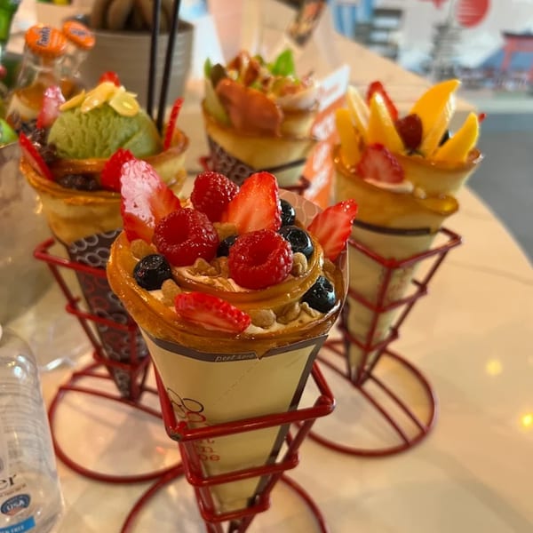 Four Eight Turn Crepes, each with different fruit and ice cream toppings, in red wire stands.