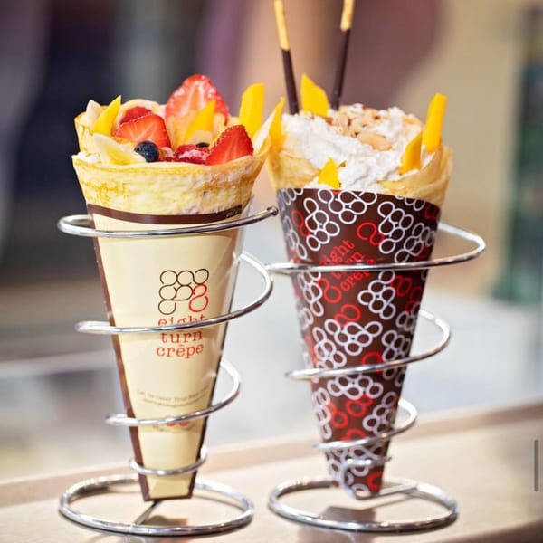 Two Eight Turn Crepes, one with fruit and one with whipped cream and mango, in metal holders.