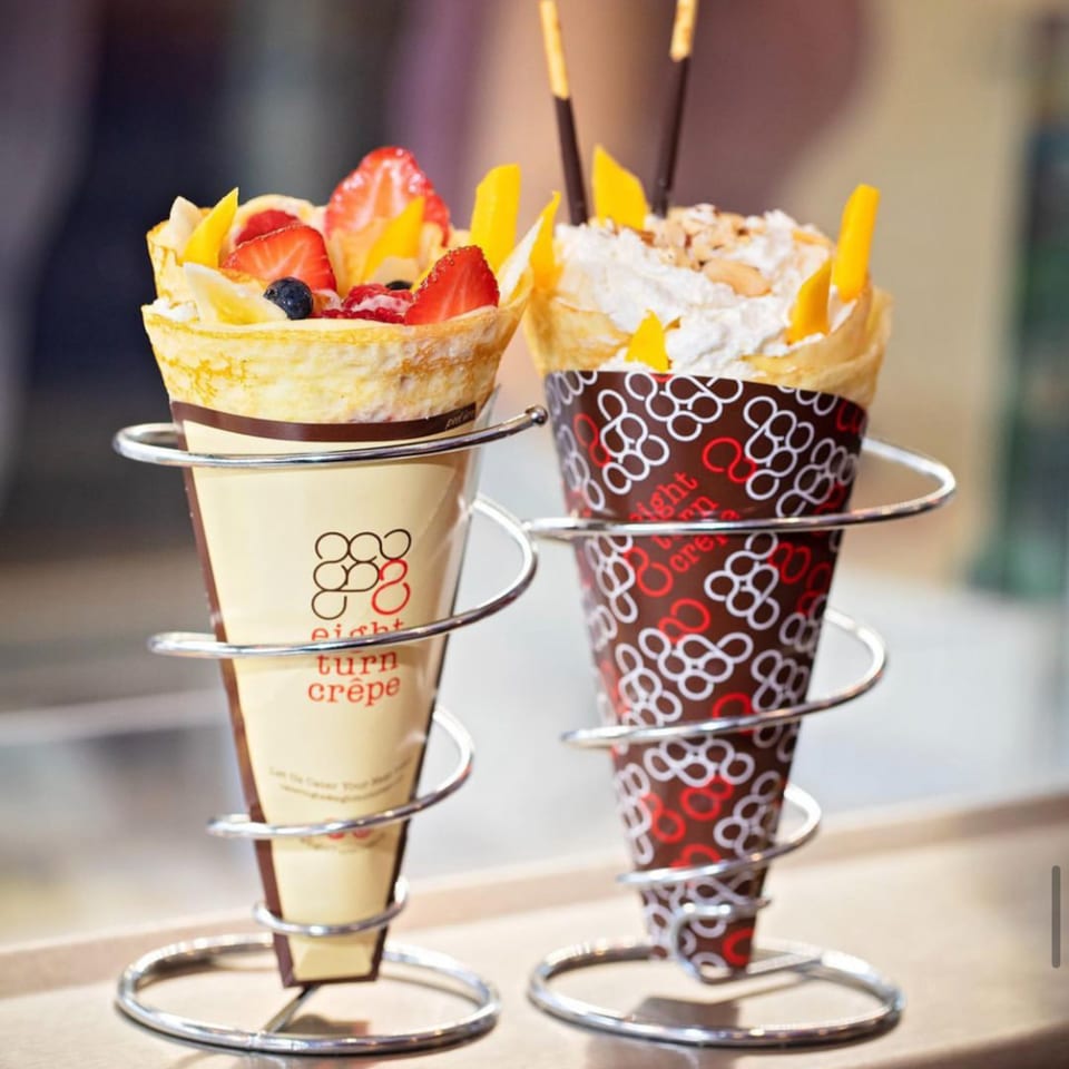 Two Eight Turn Crepes, one with fruit and one with whipped cream and mango, in metal holders.