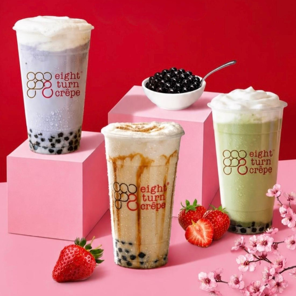 Three Eight Turn Crêpe bubble tea drinks with tapioca pearls, whipped cream, strawberries, and cherry blossoms against a red and pink backdrop.