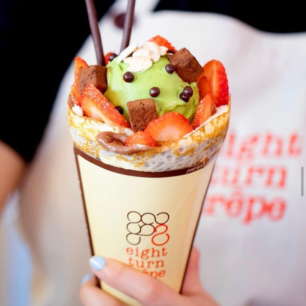 Hand holding an Eight Turn Crepe with matcha ice cream, strawberries, chocolate, and almonds.