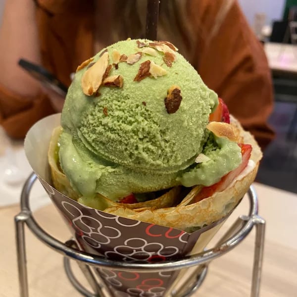 Matcha ice cream crepe with sliced almonds and strawberries in a holder at Eight Turn Crepe.