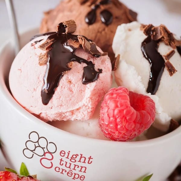 Three scoops of ice cream, chocolate, strawberry, and vanilla, with chocolate drizzle and raspberries.