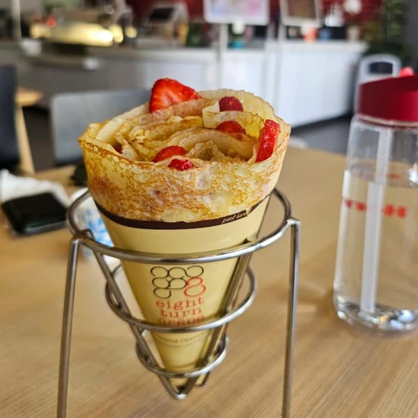 An Eight Turn Crepe with strawberries in a metal holder on a wooden table.