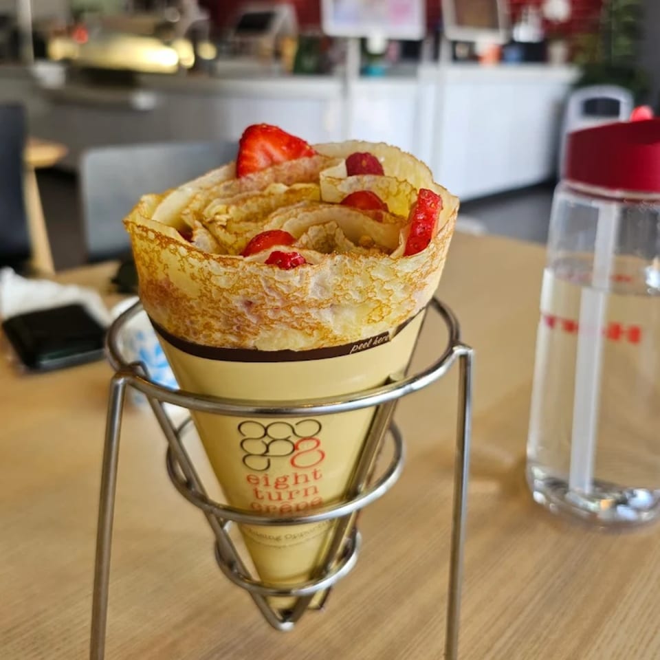 An Eight Turn Crepe with strawberries in a metal holder on a wooden table.