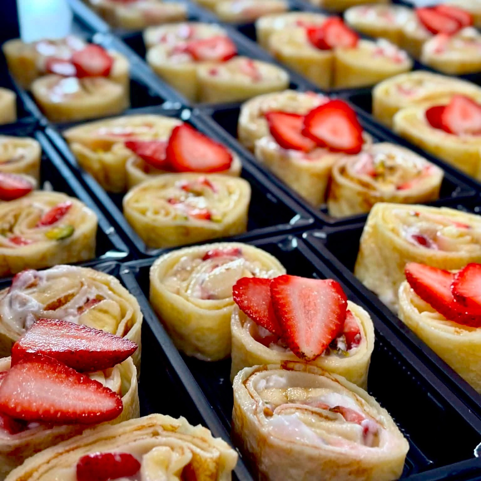 Sliced crepe rolls filled with cream and strawberries arranged in black serving trays.