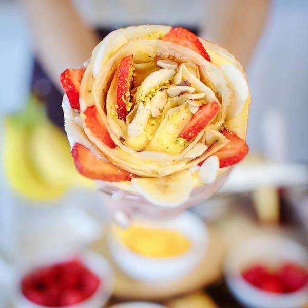 A person holding an Eight Turn Crepe filled with strawberries, bananas, nuts, and cream.