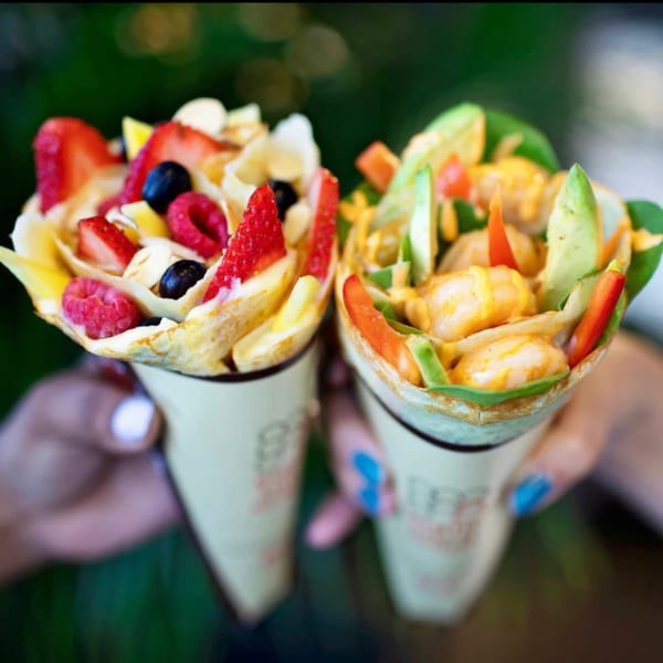 Two hands holding sweet and savory crepes from Eight Turn Crepe, filled with fresh ingredients.